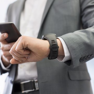 man in suit checking time smartwatch holding smartphone